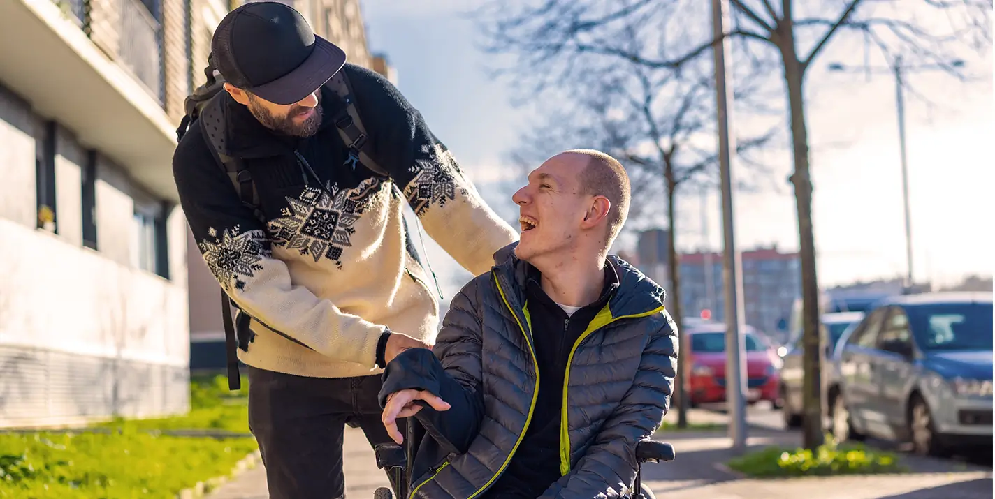 A man in a wheelchair smiling at the man next to him on street